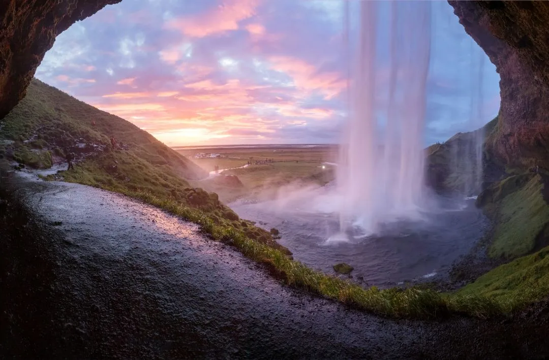 Vista da cachoeira Seljalandsfoss ao pôr do sol na Islândia, fotografada por trás da queda d’água.