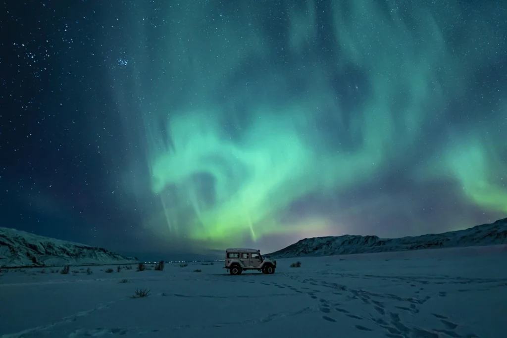 Jipe estacionado em paisagem nevada sob aurora boreal no céu noturno da Islândia.