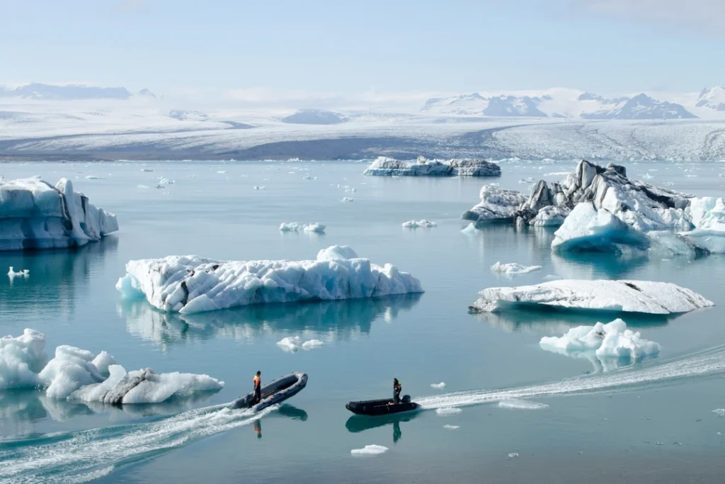 Barcos navegando entre icebergs em lagoa glacial cercada por montanhas nevadas na Islândia.