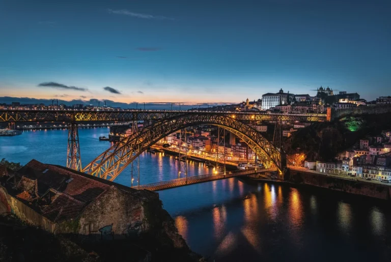 Vista da Ponte Luís I iluminada ao anoitecer sobre o rio Douro, com a cidade do Porto ao fundo.
