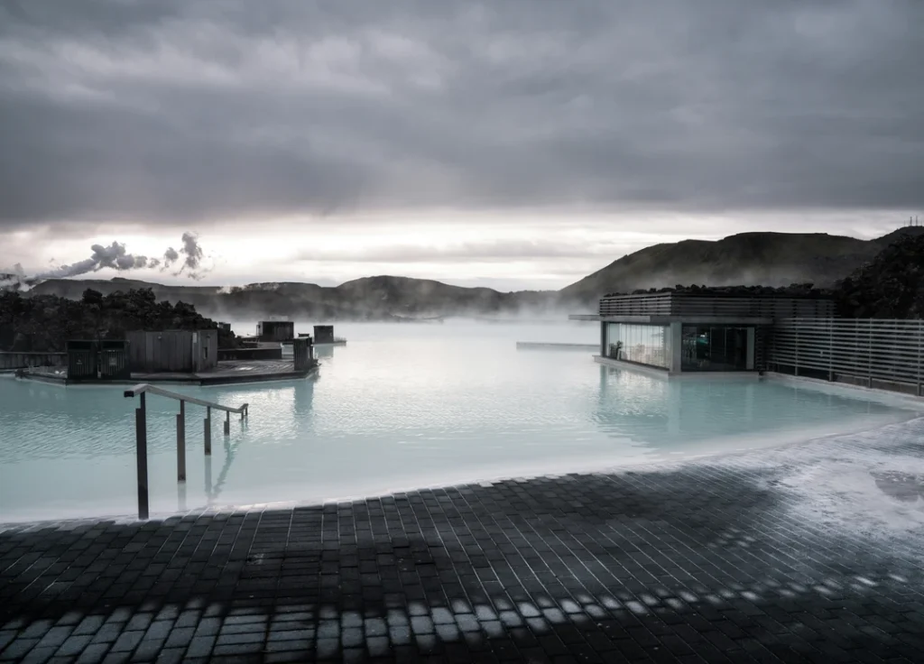 Área do spa geotérmico Blue Lagoon cercada por vapor, arquitetura moderna e montanhas ao fundo na Islândia.