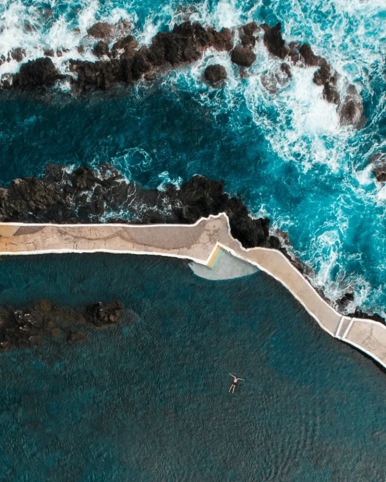 Vista aérea de piscinas naturais nos Açores junto ao oceano Atlântico, rodeadas por formações rochosas vulcânicas.